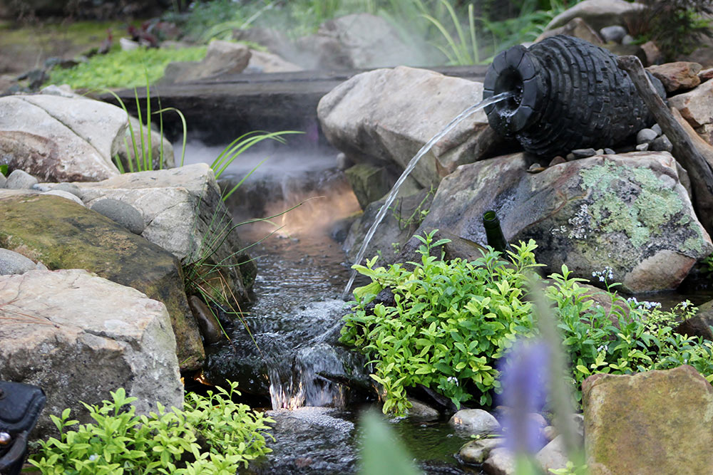 Custom garden fountainscape with urn fountain, waterfall, and natural rock borders